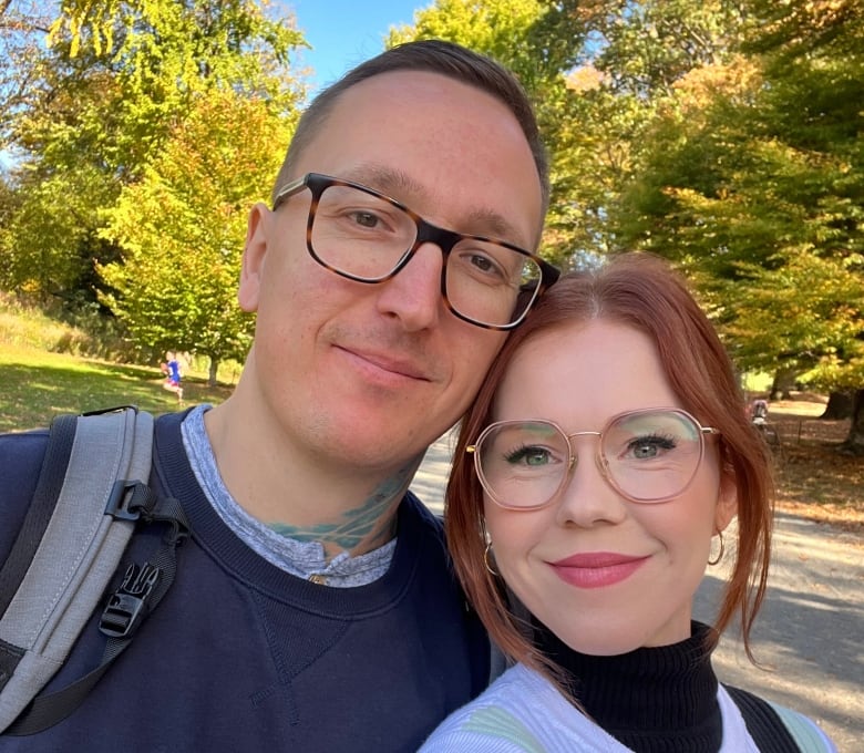 A man and a woman both wearing glasses lean their heads together and smile at the camera.