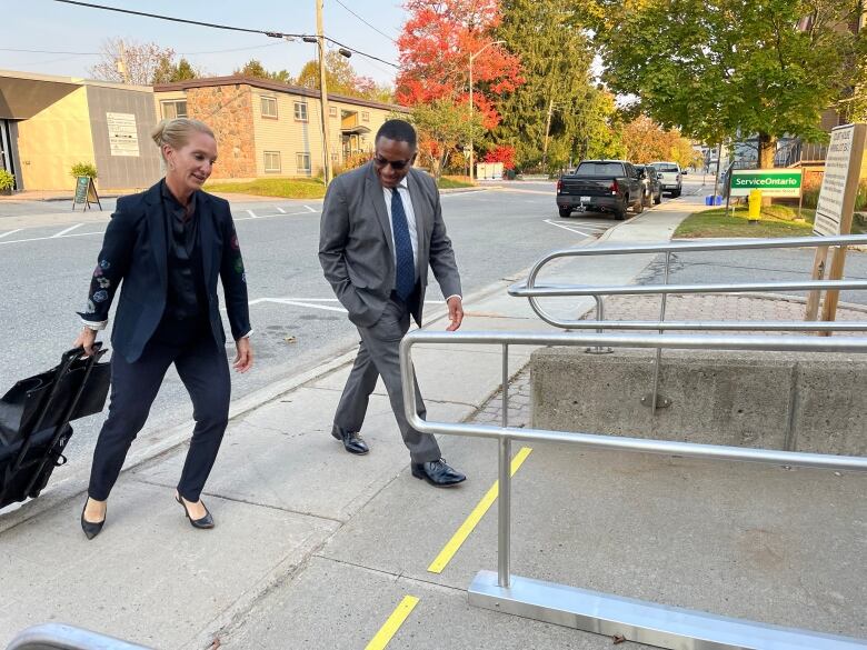 A man and a woman dressed in formal clothing walk on a sidewalk.