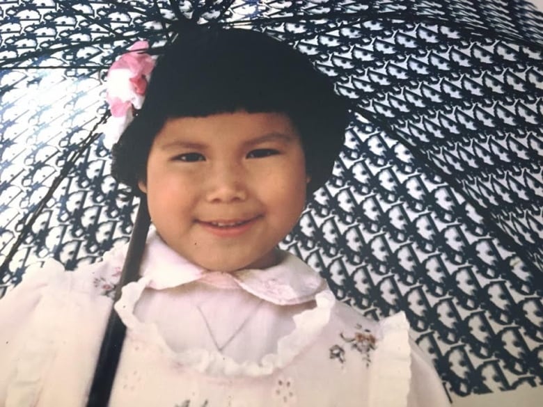 A young girl with a pink and white flower in her short dark hair holds an umbrella 