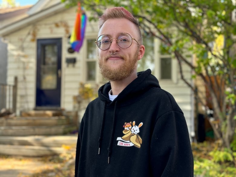 A man in front of a house with a pride flag.