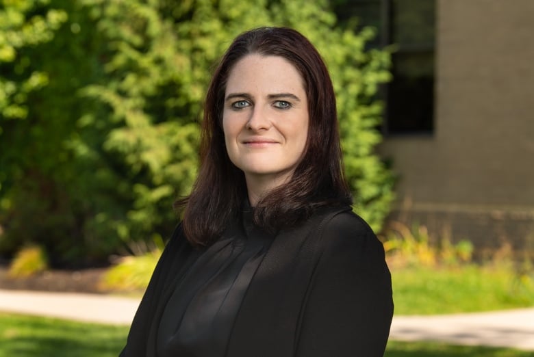 A woman with dark hair and wearing dark clothes poses for a portrait outside.