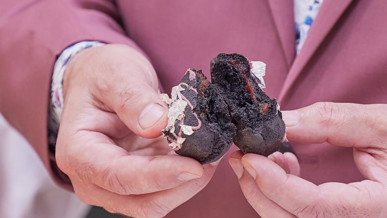 A close-up of a man's hands breaking a thick chocolate cookie in half revealing a red jam filling inside.