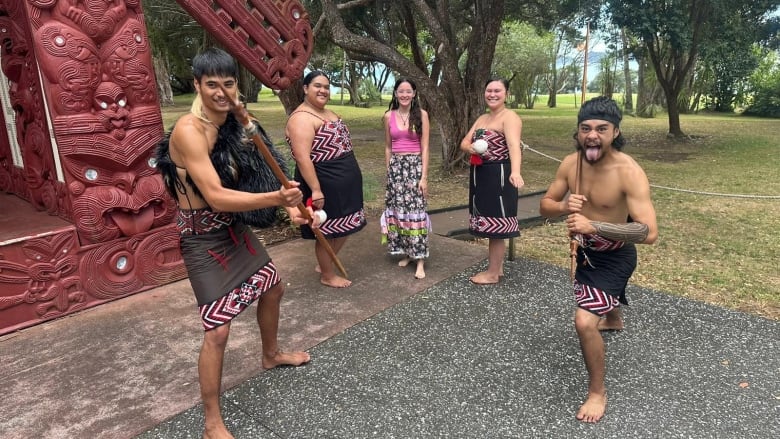 Four Maori people in regalia with a woman in a long skirt and pink tanktop in the middle. 