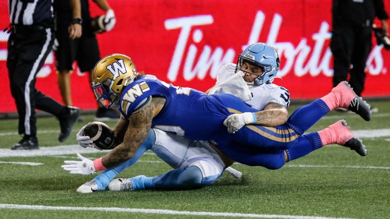 A ball-carrier in blue stretches out while being tackled by an opposing player in white.