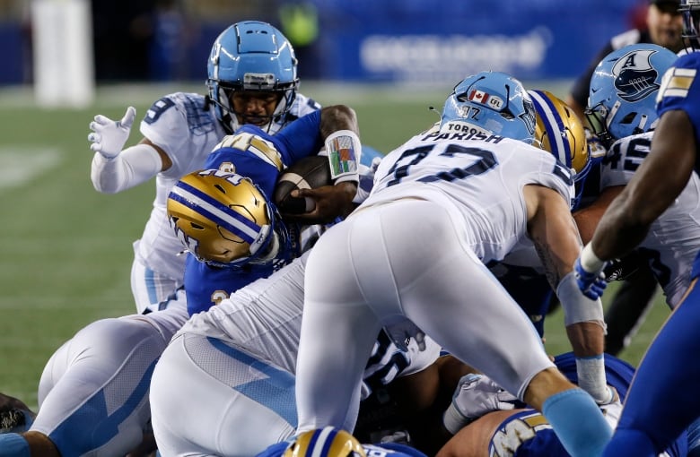 A ball-carrier in blue is tackled by three players in white.