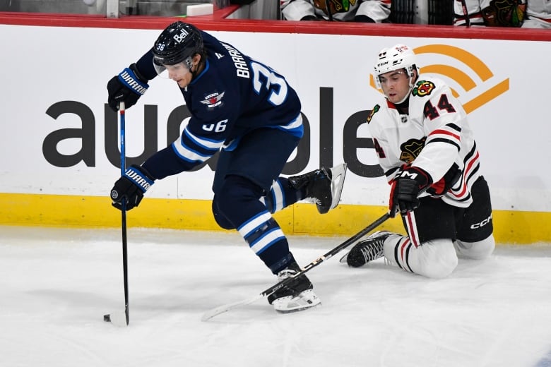 A puck-carrier in blue skates away from a player in white, who stretches his stick out while on his knees.