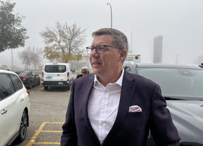 A man in a suit stands outside in a parking lot.