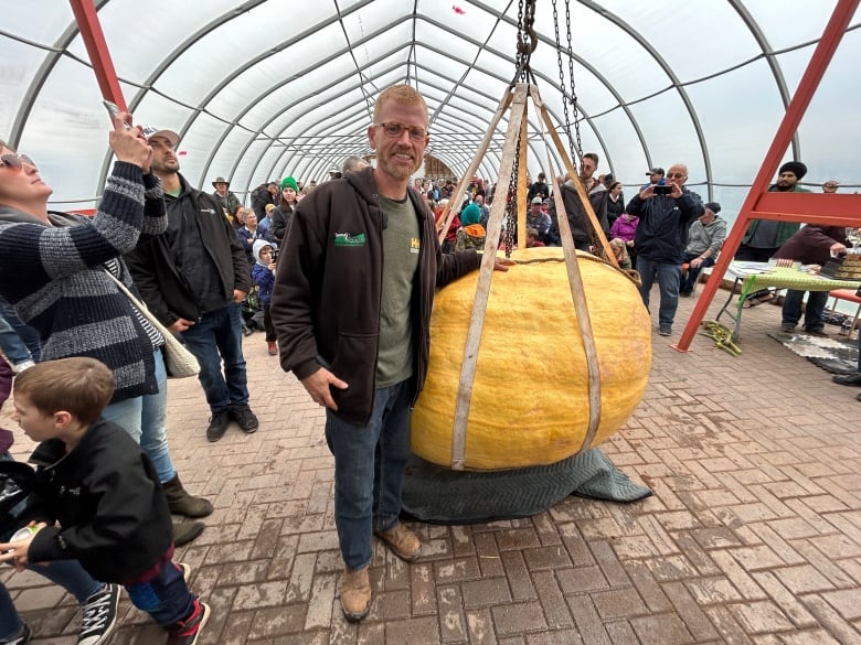 Man standing beside large yellow pumpkin.