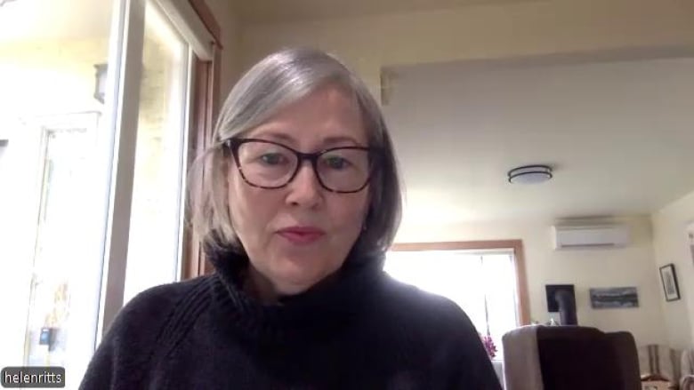 A woman with grey hair and glasses is seen in a house on a video call on her computer.