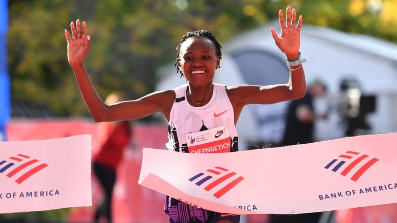 A female marathon competitor smiles while raising both arms in celebration as she breaks the finish line barrier.