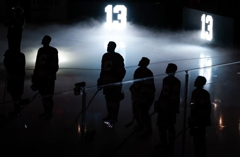 Hockey players are shrouded in darkness as the number 13 is displayed behind them.