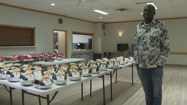 A man stands next to multiple tables with many uncooked turkeys