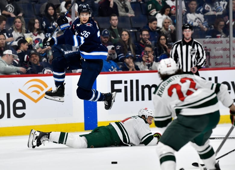 A hockey plater mid air while another is laying on the ice