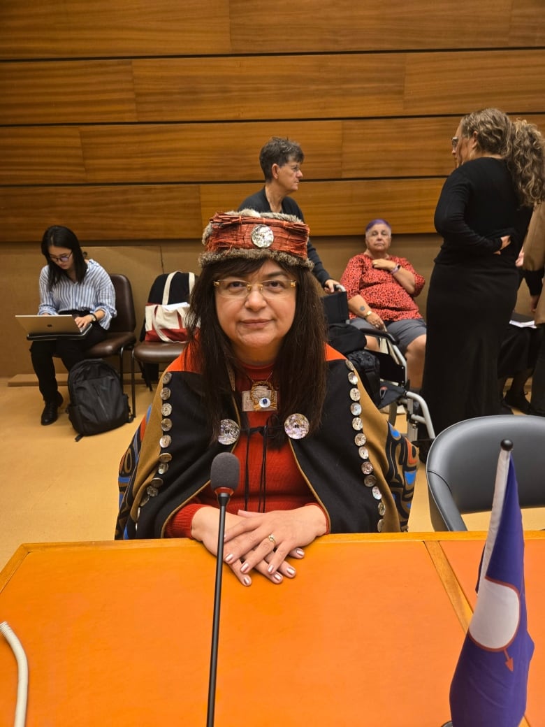 An Indigenous woman smiles as she sits at a desk, as others are seen behind her.