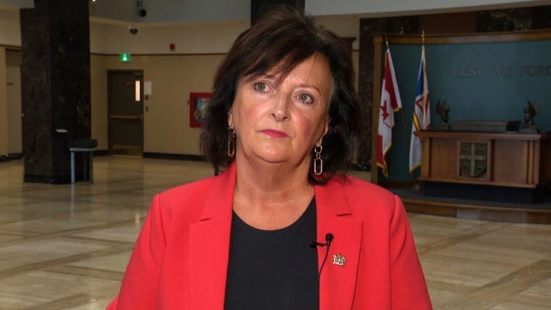 A woman wearing a red jacket and a black shirt standing in a lobby. 