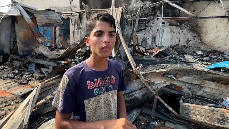 A young boy stands in the middle of a destroyed tent camp site.