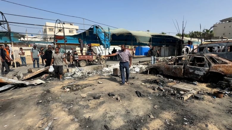 A man stands, pointing at a destroyed tent camp site.