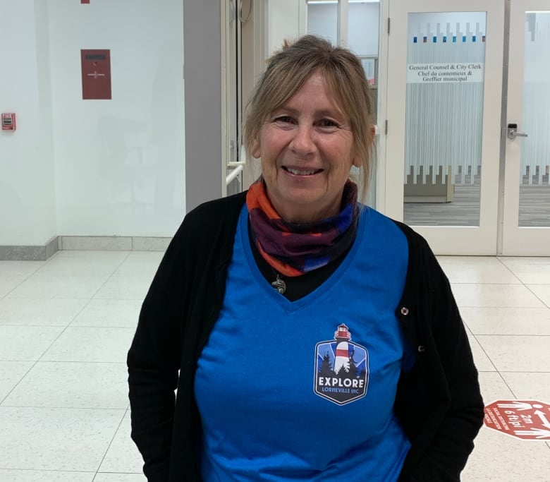 Woman, wearing blue t-shirt with black cardigan, smiling at camera. 