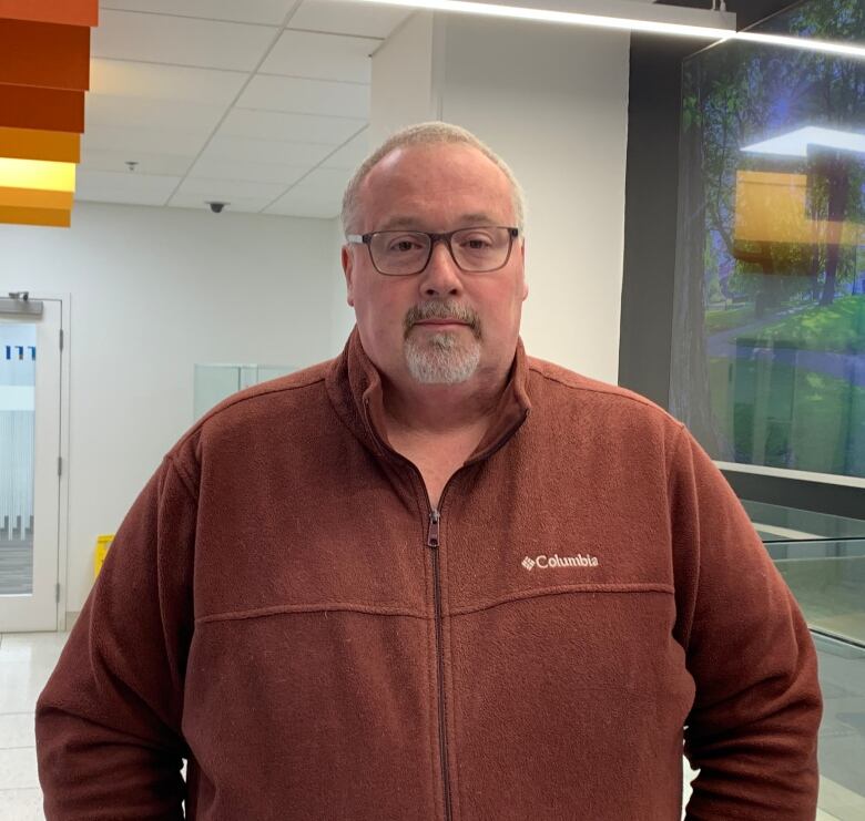 Man wearing reddish brown sweater with glasses looking at camera with a neutral expression.