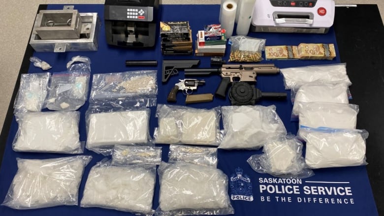 Bags of white powdery drugs, handguns, bills of money, electronics displayed on top of a table.