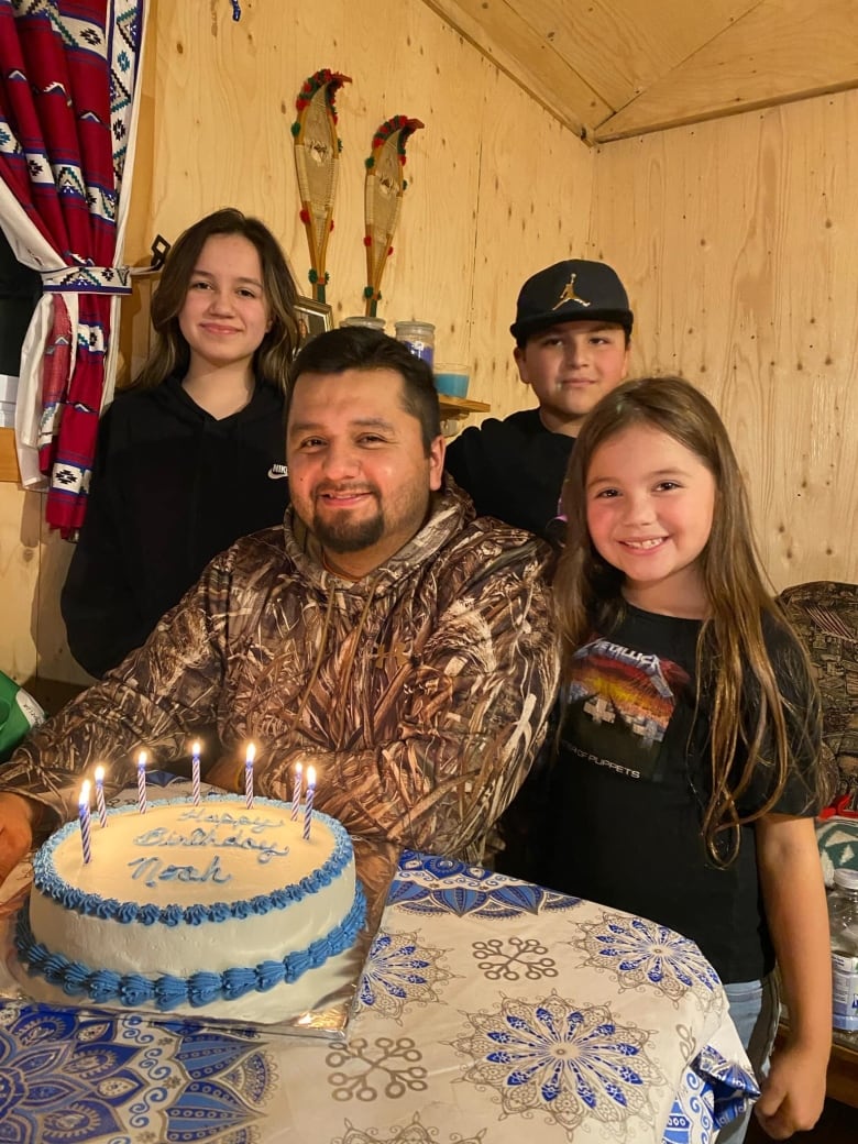 A man blowing up birthday candles, surrounded by children. 