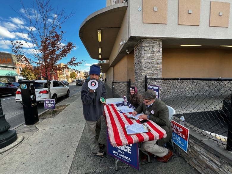 Man holds bullhorn at table of Republicans on sidewalk