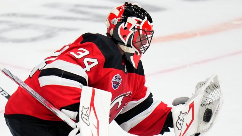 A goaltender in a New Jerseys Devils jersey mid-play with a puck in his glove