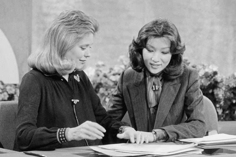 A black and white photo of two women sit at a table reviewing papers together.