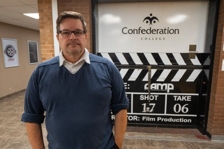 A man poses for a photo in front of a Confederation College logo.