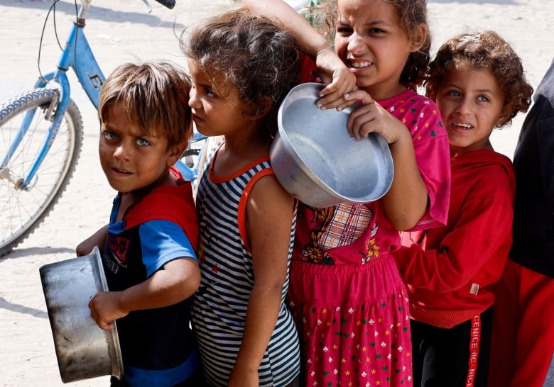 Four children stand in line holding empty bowls. 