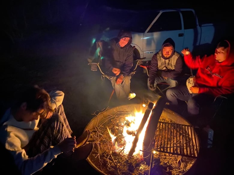 Three teenagers sitting around a campfire at night with an elderly man