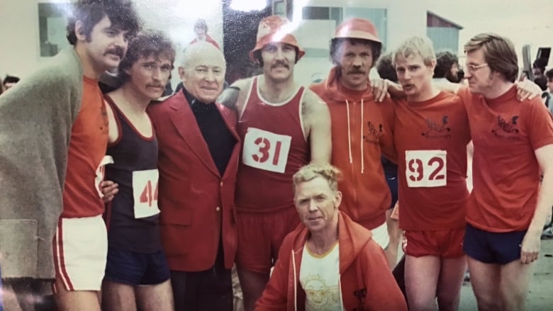 Several men in running gear and race numbers posed in a row in a 1970's photo.