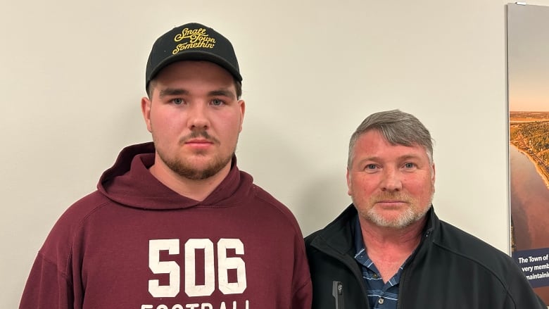 A white man with brown hair in a hoodie and hat, standing next to a white man with white hair wearing a black jacket.