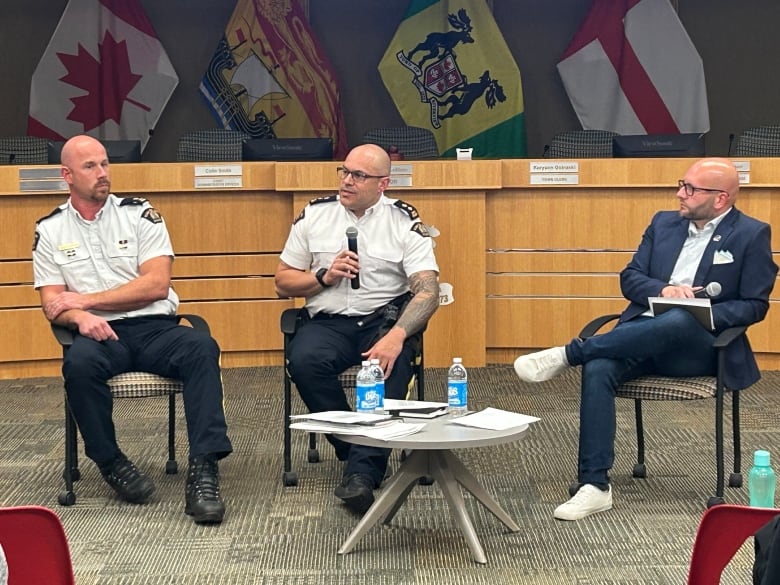 Three white men sitting next to each other. Two on the left in police uniforms and one the right in a blue suit. 