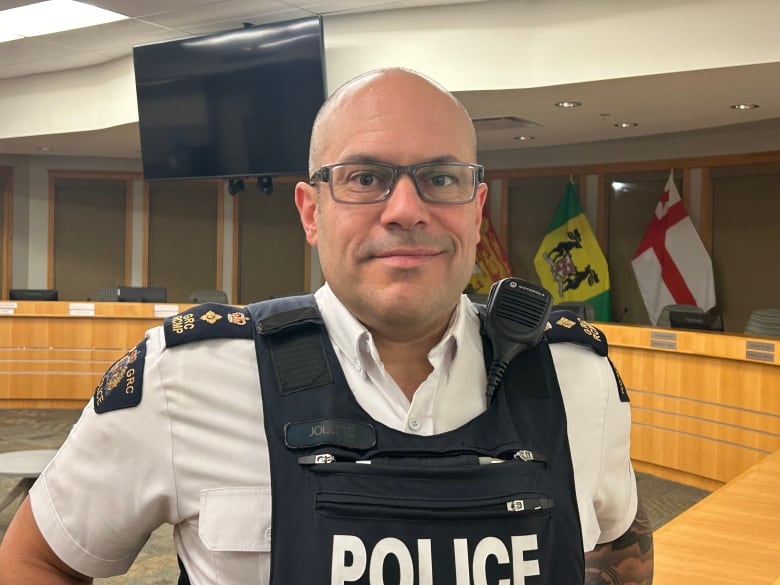 A white man in a police uniform, has no hair, wears glasses.