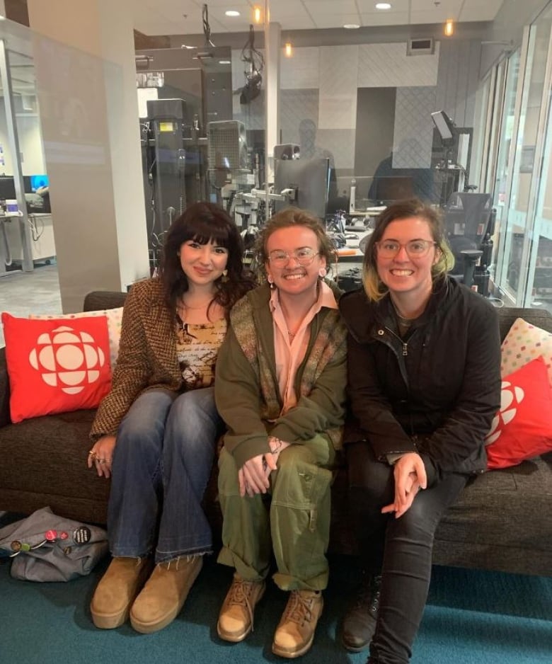 Three people sitting on a couch in a studio.