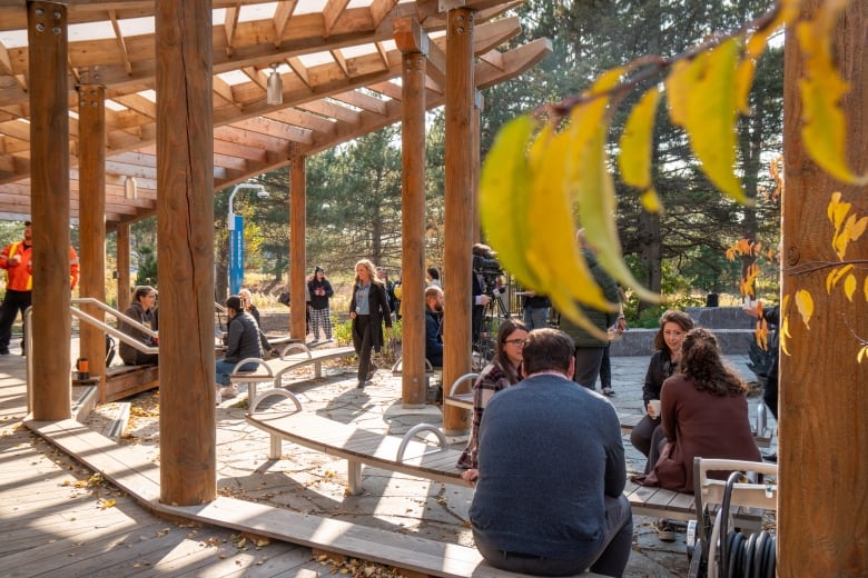 People are seen sitting and standing around a large wooden structure outside.