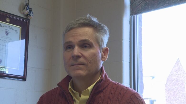 A man in a red sweater sits in an office.