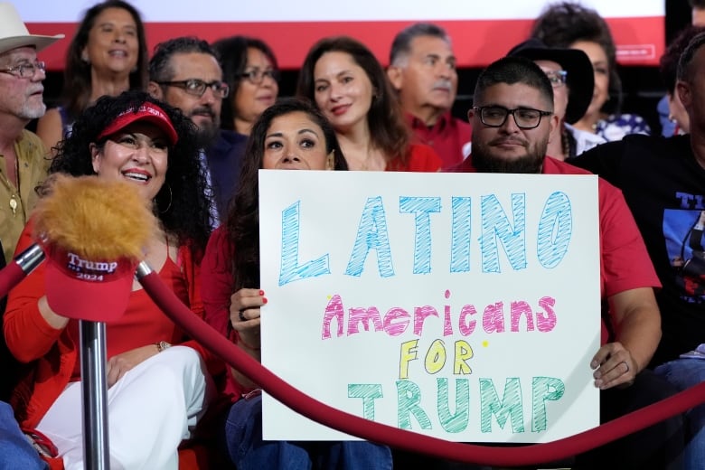 People dressed in red Trump paraphernalia hold a sign than says 