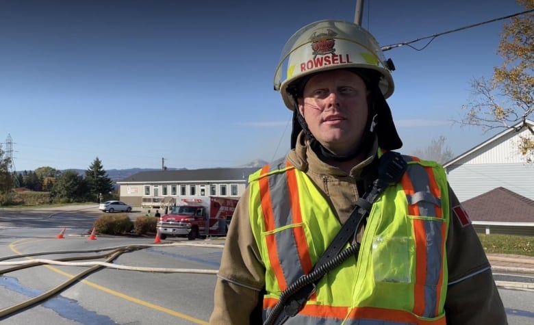 Firefighter with helmet that says Rowsell on it. Behind him is a firetruck and a building.