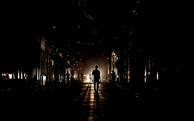 People walk down a street during a blackout as they are illuminated by a single light source behind them.