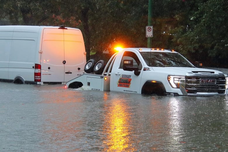 A tow truck tries to pull a white van from a flooded street.