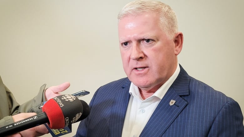 A man with white hair speaks into a microphone.