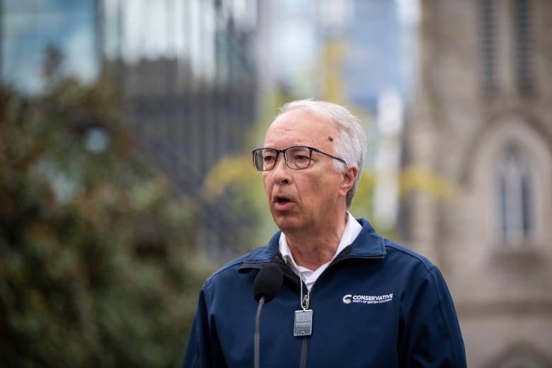 A white man wearing a blue sweatshirt talks outdoors.