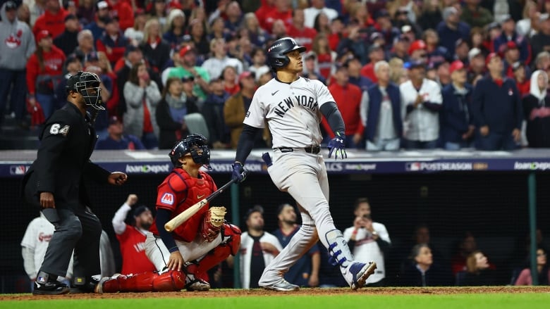 A batter is shown after his swing, watching the ball he hit. An umpire and catcher also watch the ball (not shown). 