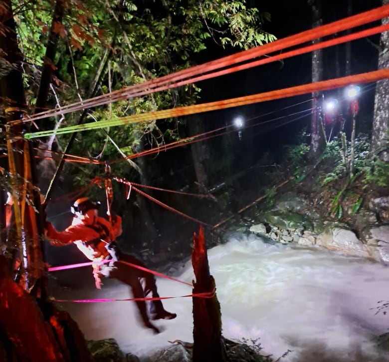 A person is seen using a highline to traverse a river at night. 