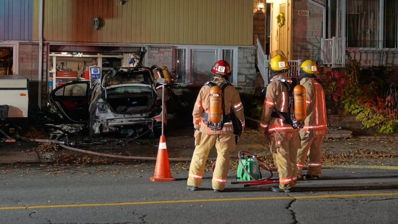 Firefighters looking at a car that was set on fire. 