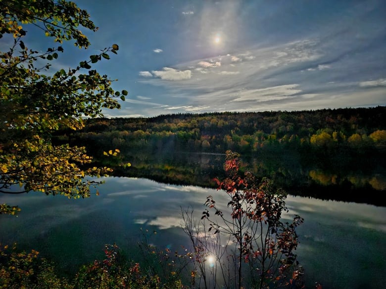 A sun and moon in sky, and reflected in river.