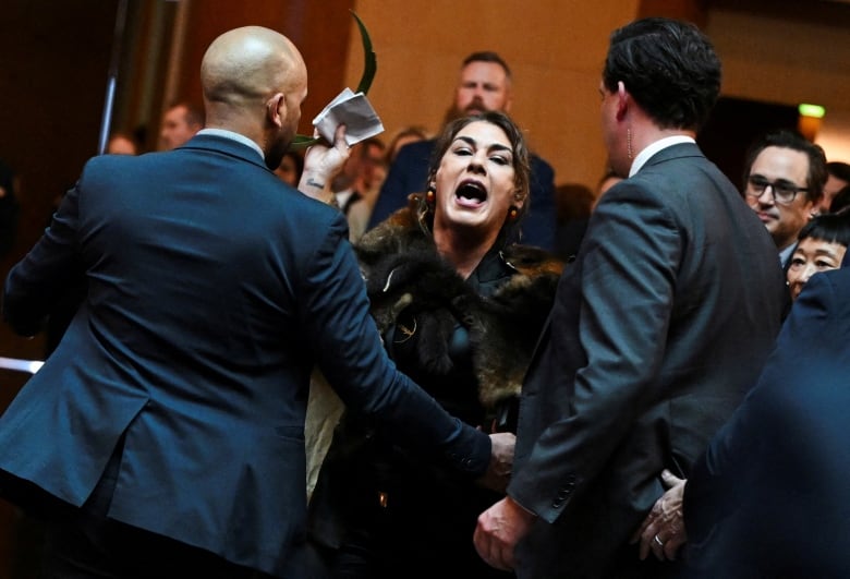 A woman is shown with her mouth open, appearing to yell, while two people stand near her.