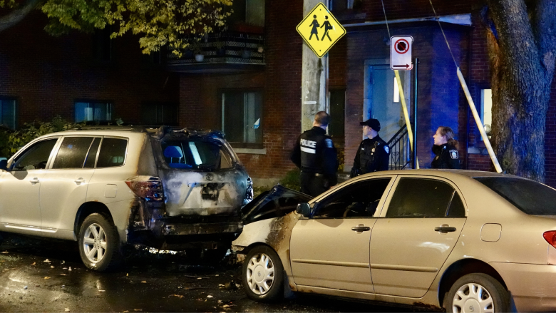 Three police officers stand beside torched cars